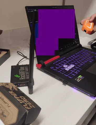 Photo of a HackRF One box on a desk next to a laptop with its screen covered by a purple redaction box.